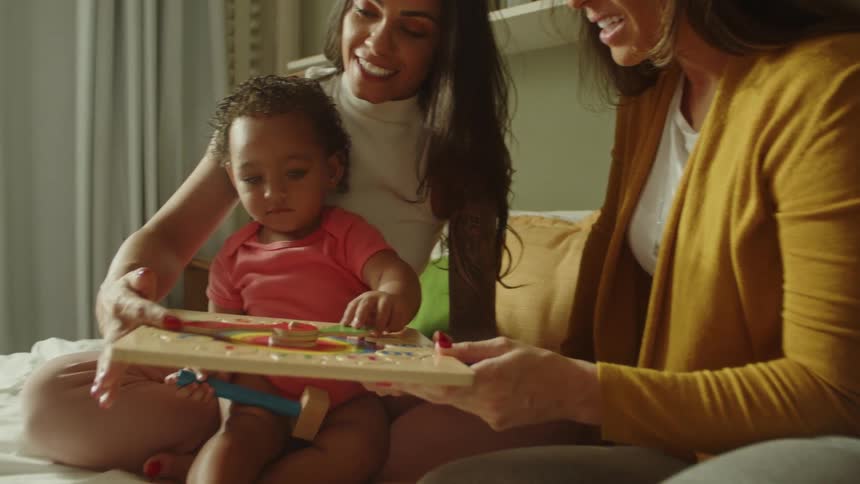 Little girl accompanied by two women playing with a toy