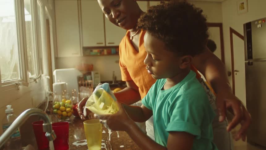 Child learns to wash dishes with mother in the kitchen