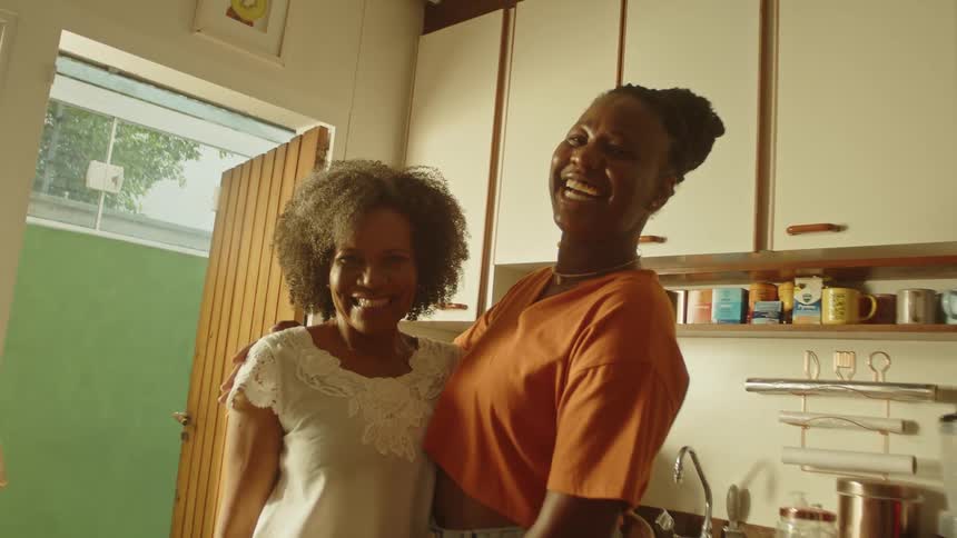 Two women stand close together and smile warmly for the camera in a cozy kitchen