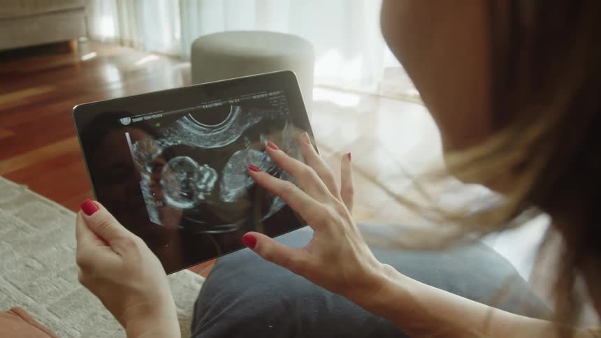 Mother smiles while looking at an ultrasound image on a tablet at home