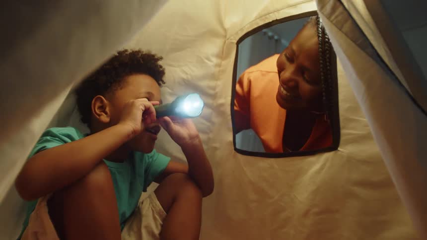 A mother talks to her son in the tent while he waves a flashlight