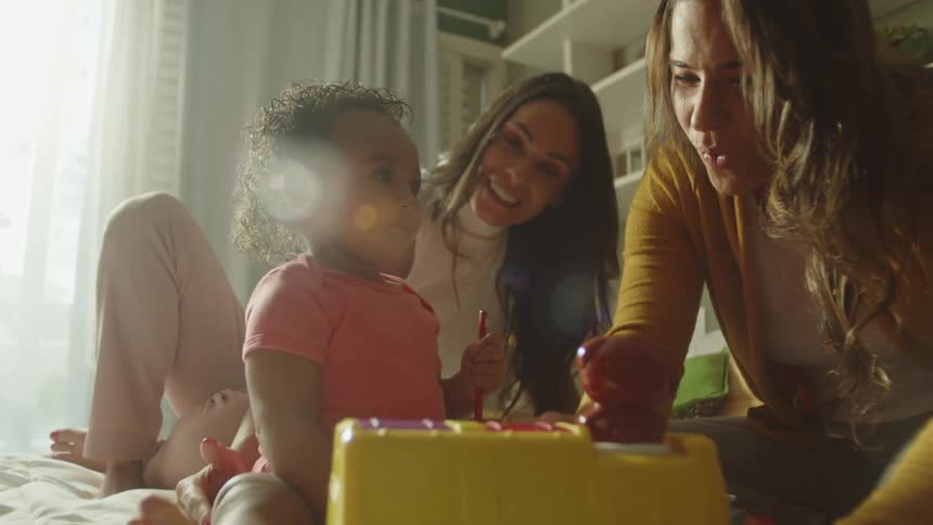 Two smiling women playing with a little girl on the bed