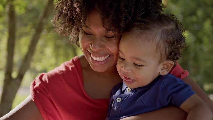 A joyful mom holds her baby boy close and theyre both smiling happily while enjoying a sunny day outside