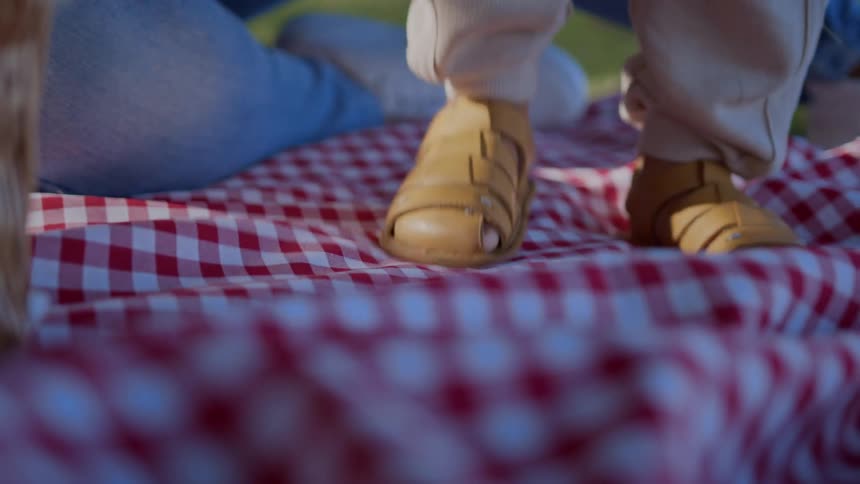 A child stomps his feet repeatedly outside on a picnic blanket
