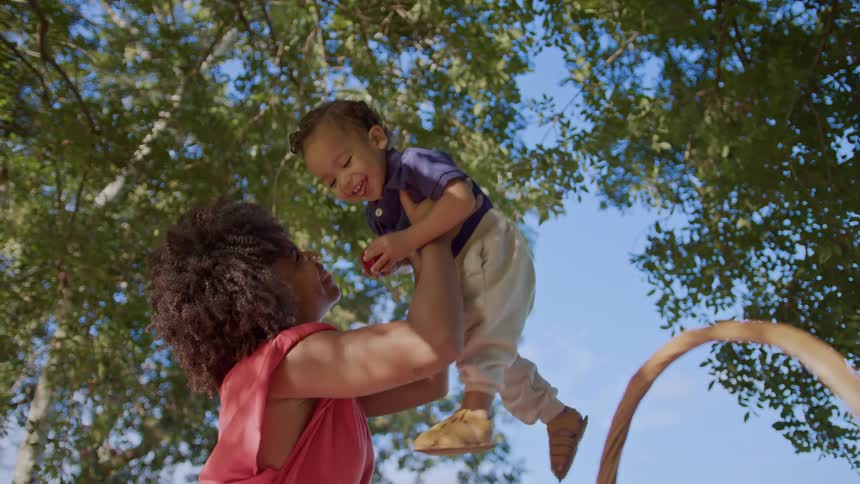 Mother and son smile while the woman lifts her child into the air during an outdoor picnic