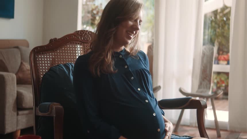 Woman in a living room with a happy expression and touching her pregnant belly
