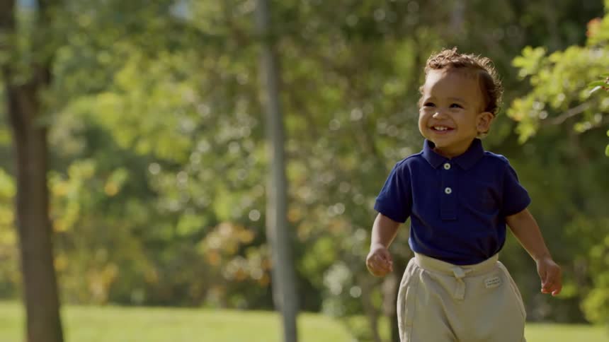 A happy toddler walks outdoors smiling brightly on a sunny day