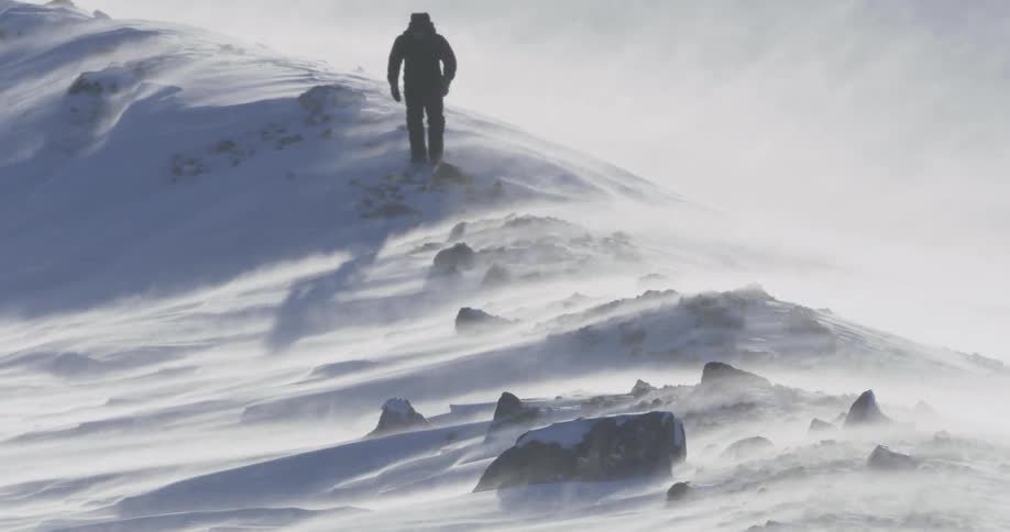 Man walking through snow covered wilderness on windy day