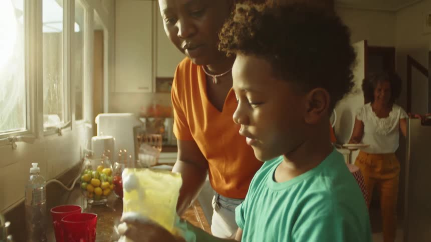 A mother and son wash dishes together at the kitchen sink