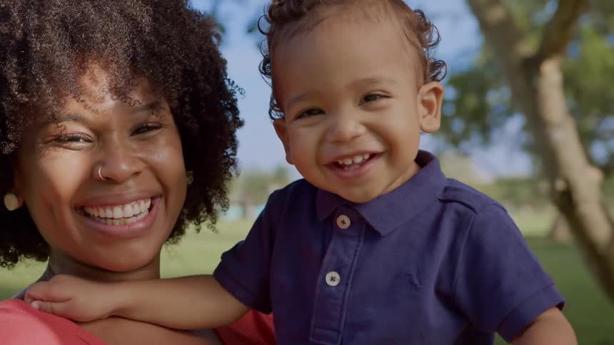 A black female holding a small child both are laughing and smiling while standing outdoors