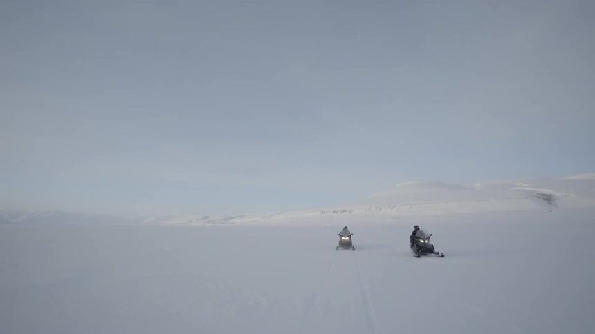 Two people ride snowmobiles in the snow