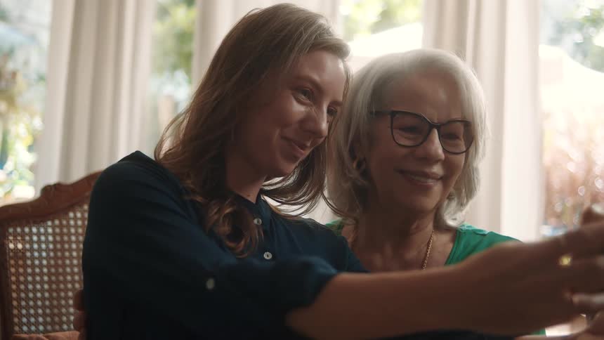 Two women smile while taking a selfie indoors near a window