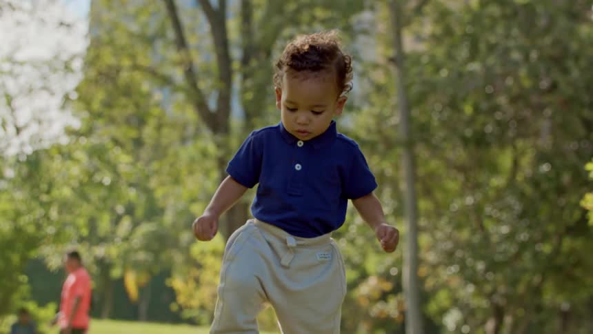 A toddler walks towards the camera in a park
