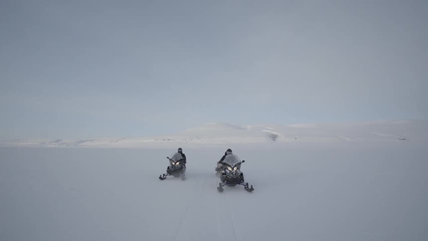 Two people are racing in the snow with snow mobiles