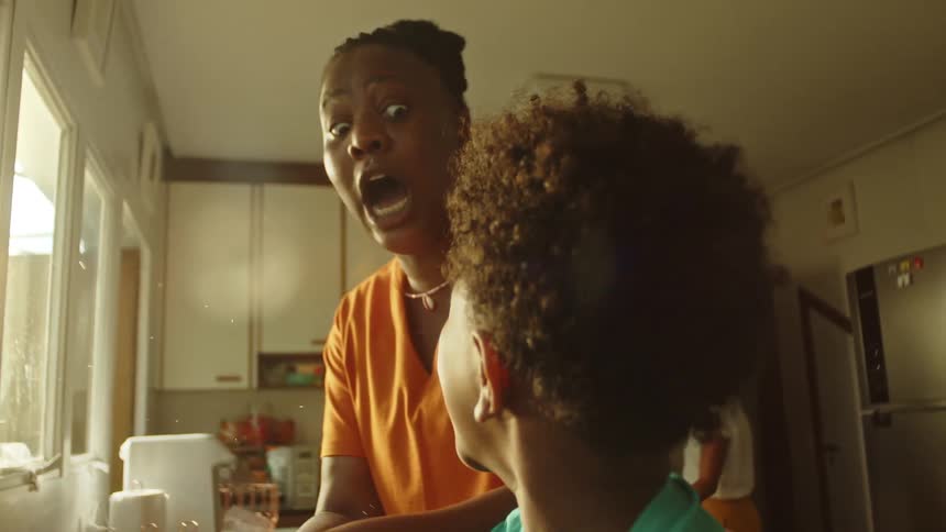 Boy accompanied by his mother washing dishes and his grandmother in the background