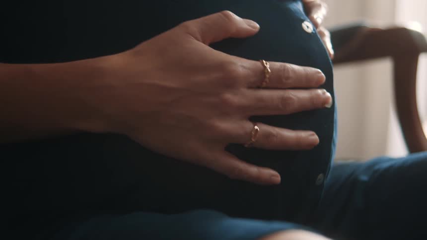 A woman sitting on a chair is rubbing her pregnant belly