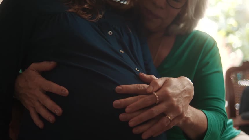 A mother is sitting with her daughter and rubbing her pregnant belly