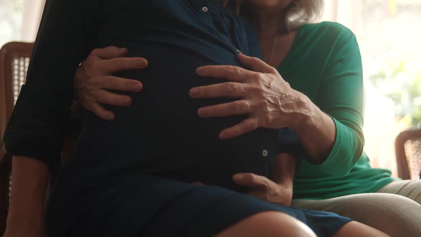A mother is hugging her daughter and rubbing her pregnant belly