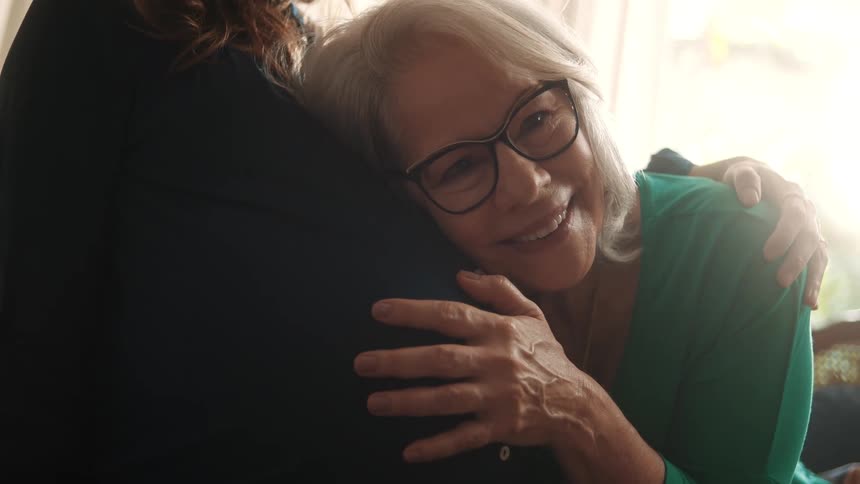Elderly woman lovingly hugging pregnant womans belly