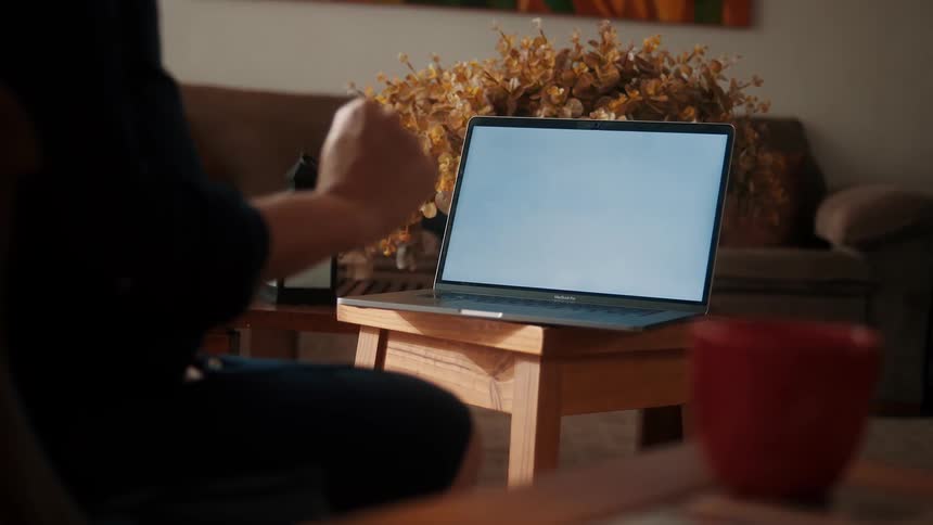 A person gestures near a laptop on a small table in a cozy living room