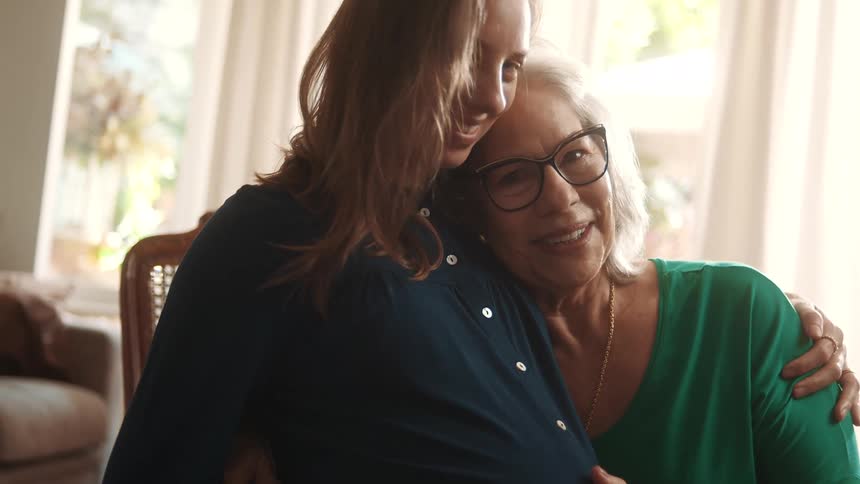 An older woman lovingly embraces a pregnant woman while resting her hand on her belly