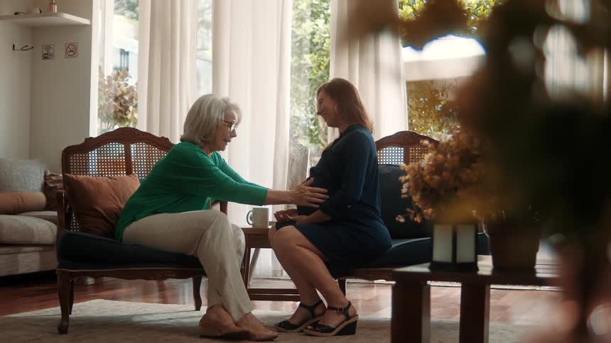 Lady sitting next to a pregnant woman and both in a happy moment holding hands