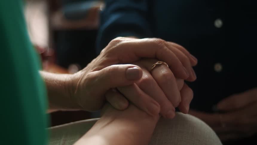 An elderly hand gently holds a younger hand in a comforting gesture