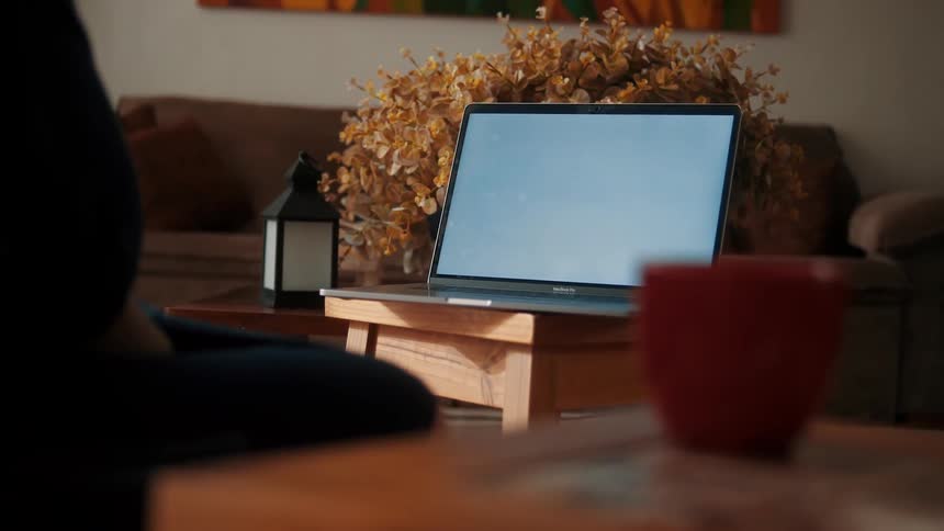 Pregnant woman leans forward to tap her laptop keyboard while sitting in the living room