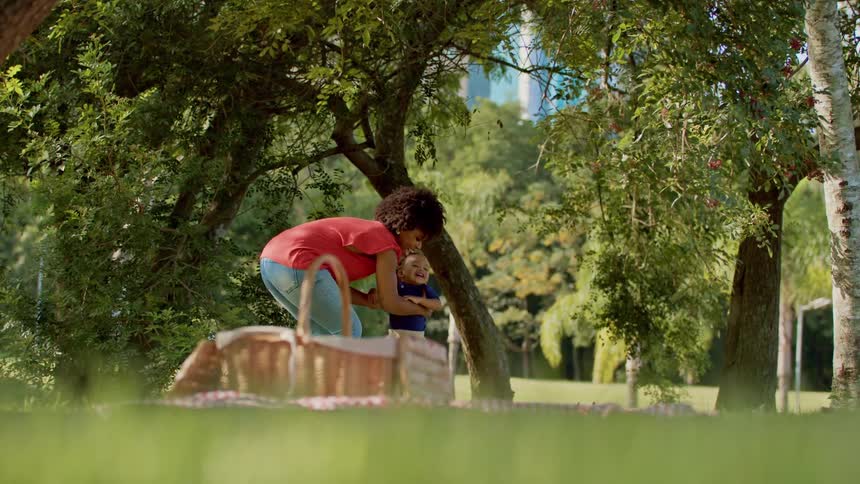 A mother helps her young child walk during a picnic in a lush park