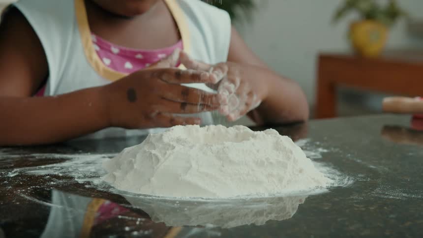 Child sitting at a table with his hands reaching for wheat flour being scattered on the table
