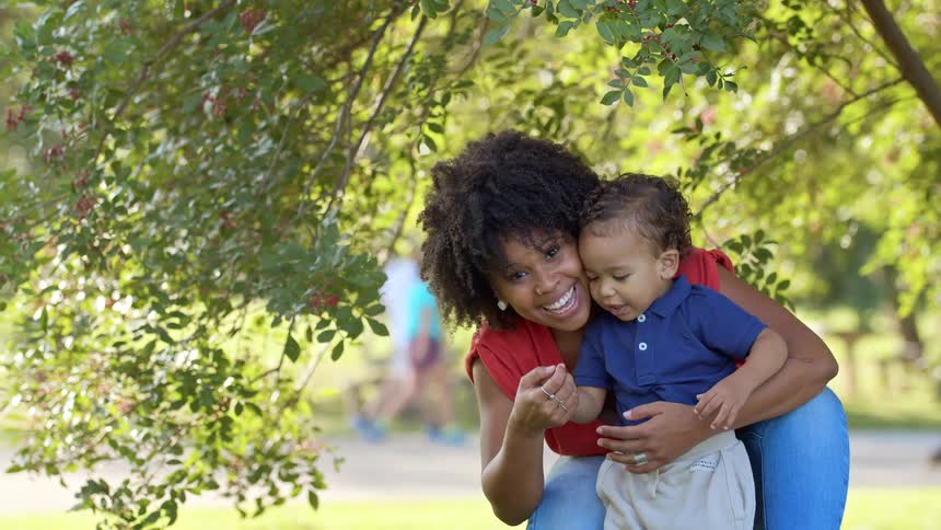 A mother holds her sons hand and smiles in the park