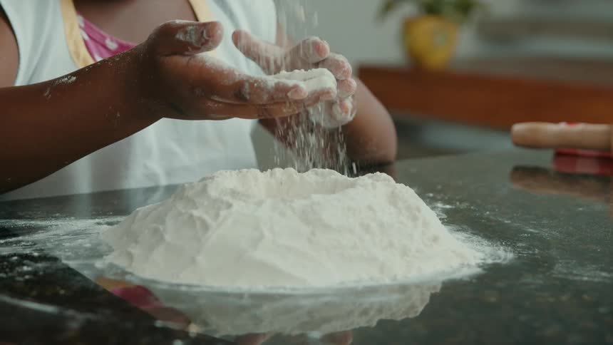 Flour falls over a set of hands and onto a pile on the countertop
