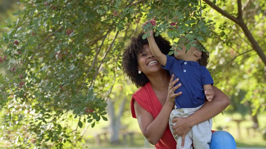 Woman lifts child to reach berries on tree