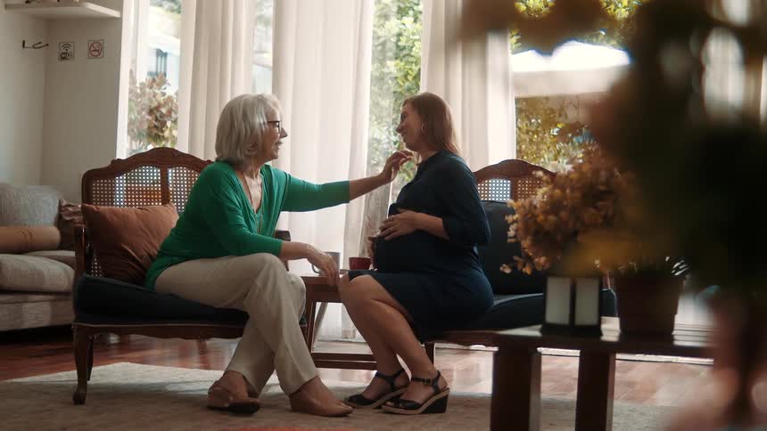 Elderly woman sitting talking to another pregnant woman