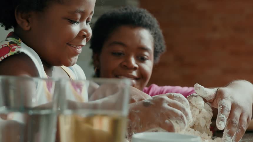 A mother and daughter are mixing the flour with their hands