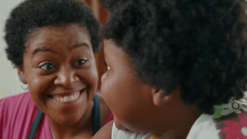Smiling mother and child stand side by side in a bright room focused on a shared activity