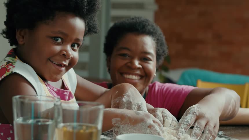 Mother and daughter smiling while mixing flours indoor with their hands