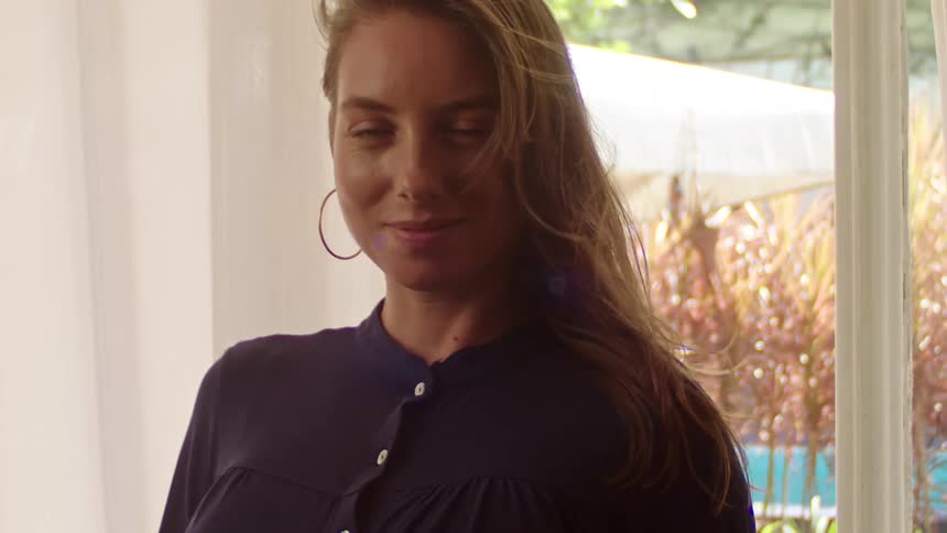 A woman smiles warmly while standing indoors near a sunlit window