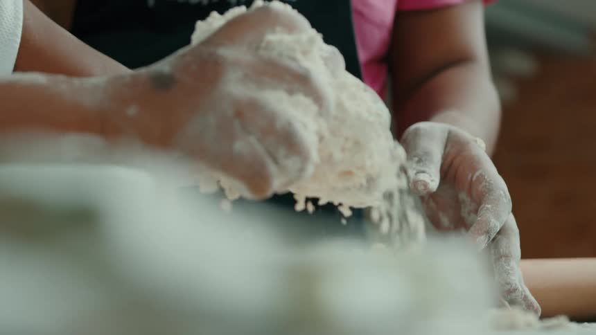 A small black child playing with dough and flour next to a person