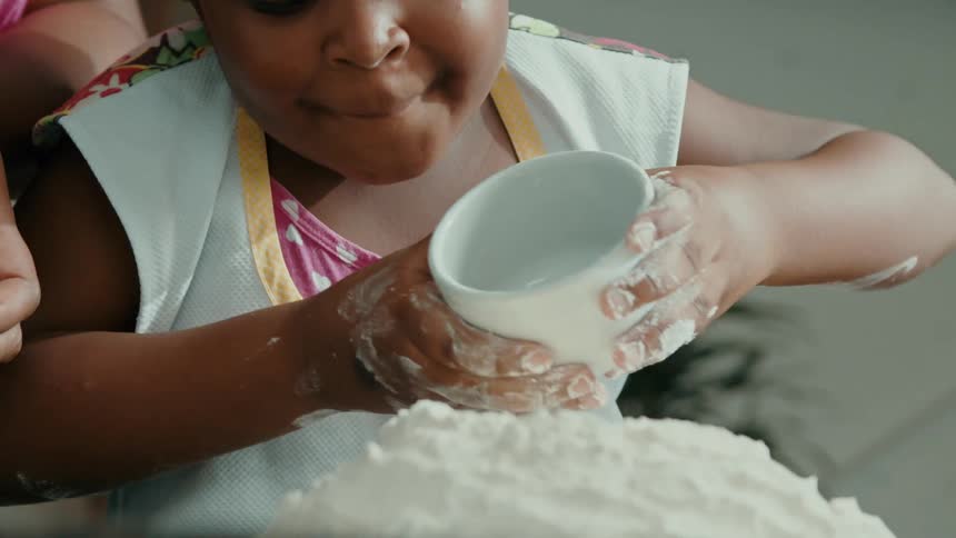 Girl pour raw egg on flour with her mother standing close