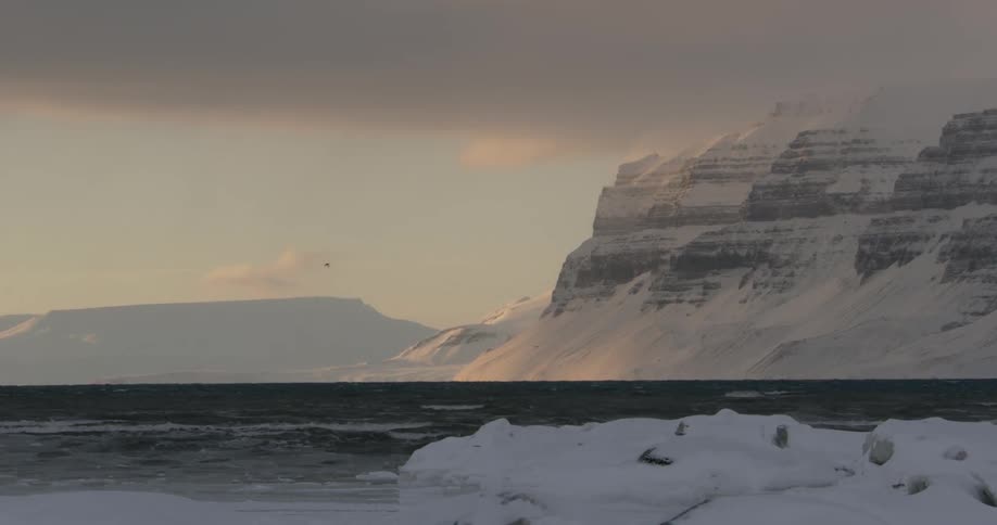 Water flowing next to a snow cliff at sunset