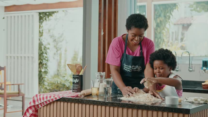 Mother helps her bring flour onto the dough for kneading on the counter