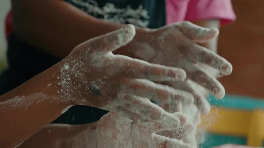 Two people clap their hands to make flour fall off onto the counter