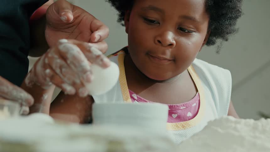 A kid molds dough in the kitchen with her mother standing behind her