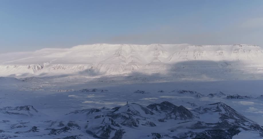 Person standing on snow covered hill surrounded by snow in the arctic