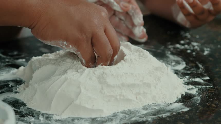 Pair of hands working with wheat flour on top of a marble surface
