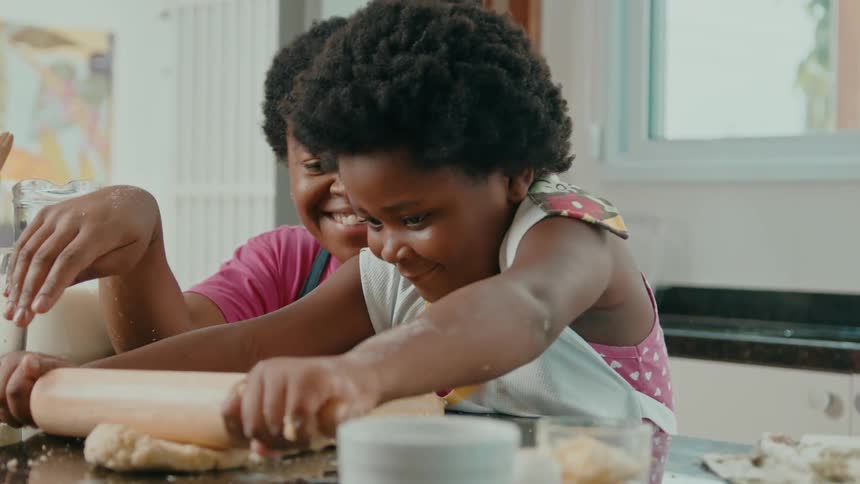 A woman and young girl smile while rolling out dough together in a kitchen