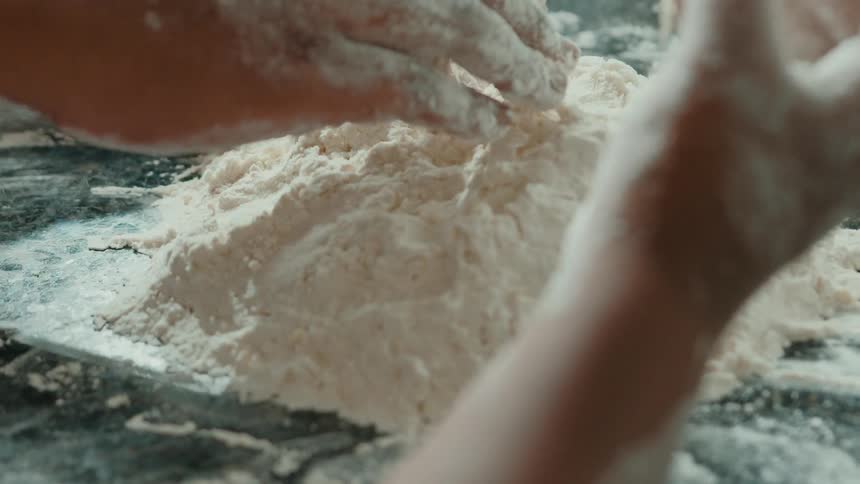 Pair of hands covered in flour patting a mound of flour on a marble counter