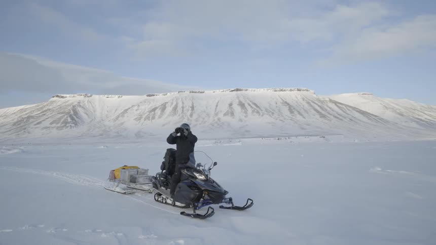 A man stops his snowmobile and looks through binoculars