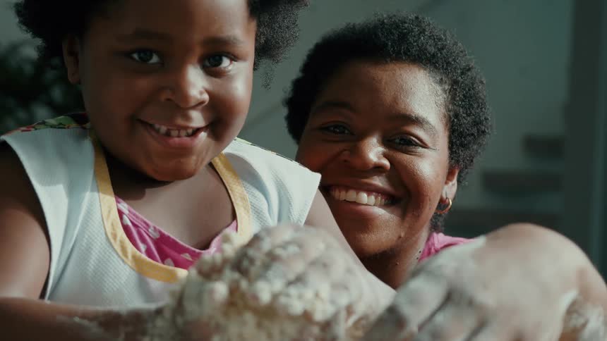 A girl and her mom smile while rolling flour in their hands